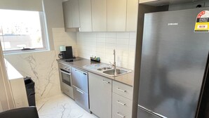 A compact kitchen with a stainless steel refrigerator, a built-in oven, and a sink. - Deluxe One Bedroom Apartment (Newcastle)