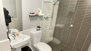 A bathroom with a white sink, toilet, and glass shower enclosure. - Deluxe One Bedroom Apartment (Newcastle)