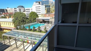 A balcony with a glass enclosure overlooking a swimming pool and buildings. - Deluxe One Bedroom Apartment (Newcastle)