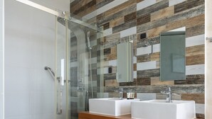 Een moderne badkamer met twee wastafels, een glazen douchecabine en een houten wastafelmeubel met opbergruimte.