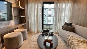 Ein modernes Wohnzimmer mit Sofa, Hocker, Couchtisch und einem Flachbildfernseher an einer Marmorwand.