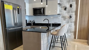 Eine moderne Küche mit einem Edelstahl-Kühlschrank, einer eingebauten Mikrowelle und einer Bar mit einer schwarzen Arbeitsplatte und einem Barhocker.