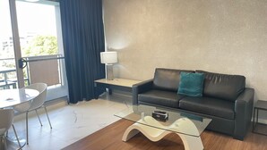 Una sala de estar moderna con un sofá, una mesa de centro de vidrio, una lámpara y un comedor con sillas.