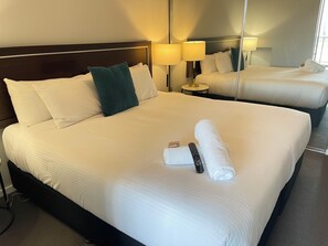 A hotel room with a large bed, two bedside lamps, a mirror, and a neatly made bed with towels and a remote control.