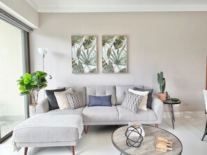 A modern living room with a grey sofa, a coffee table, and two framed botanical prints on the wall.