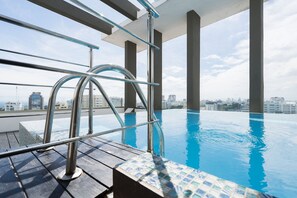 Piscina infinita interior com grades de metal, um deck de madeira e vista para a cidade ao fundo.