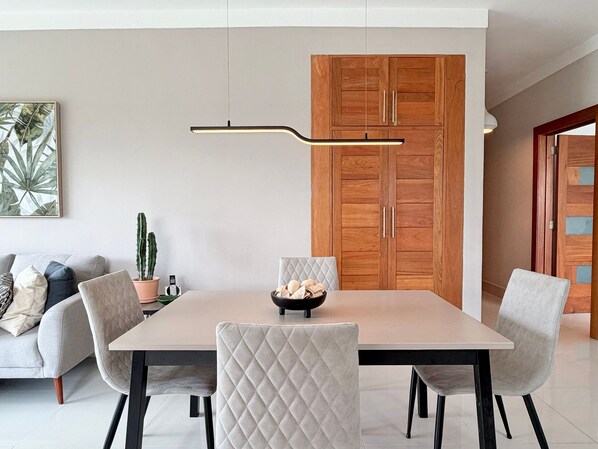 A modern dining area with a rectangular table, four chairs, a hanging light fixture, a wooden wardrobe, and a potted plant.