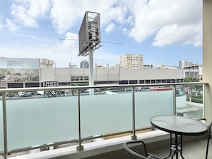 A balcony with a view of a parking lot and buildings, a table, and a chair.