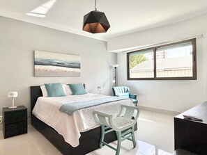A modern bedroom with a bed, a chair, a desk, and a window.