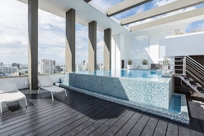 Piscina no terraço com vista clara para o horizonte da cidade, cercada por paredes brancas e arquitetura moderna.