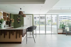 A modern reception area with a counter, bar stools, a hanging light fixture, and a view through large glass doors.