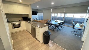 Eine moderne Küche mit Edelstahlgeräten, eine Essecke mit großem Tisch und Stühlen sowie ein Ausblick durch große Fenster.