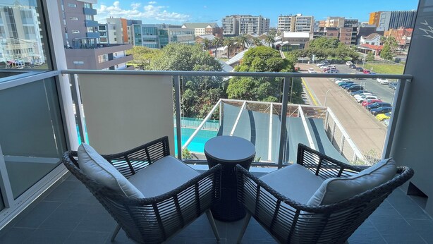 Un balcon avec des fauteuils en osier et une petite table, donnant sur un parking et des immeubles.