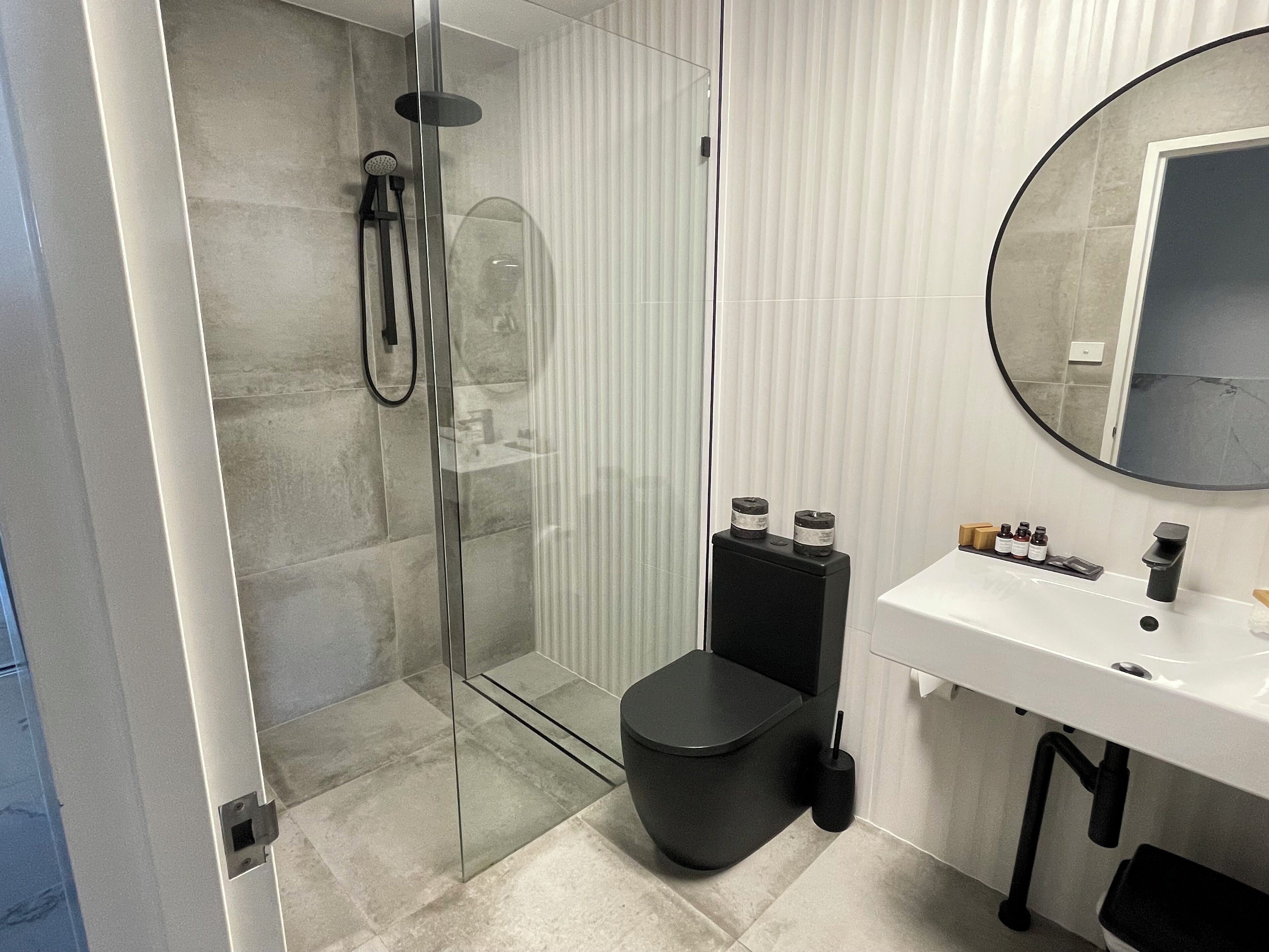 A modern bathroom with a glass-enclosed shower, a black toilet, and a white sink with toiletries.