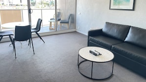 Un salon moderne avec un canapé en cuir noir, une table basse ronde et une table à manger en verre, accompagnée de chaises.