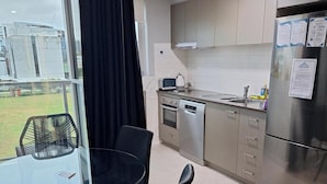 A modern kitchen with stainless steel appliances, a glass dining table, and a view of the outdoors. - Prestige One Bedroom (Newcastle)