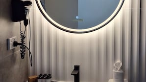 A bathroom with a round mirror, a hairdryer, a sink, and toiletries. - Prestige One Bedroom (Newcastle)
