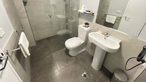 A modern bathroom with a glass-enclosed shower, a toilet, a sink, and a mirror. - Standard One Bedroom (Newcastle)