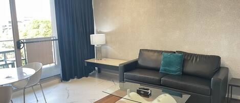Una sala de estar moderna con un sofá, una mesa de centro de vidrio, una lámpara y un comedor con sillas.