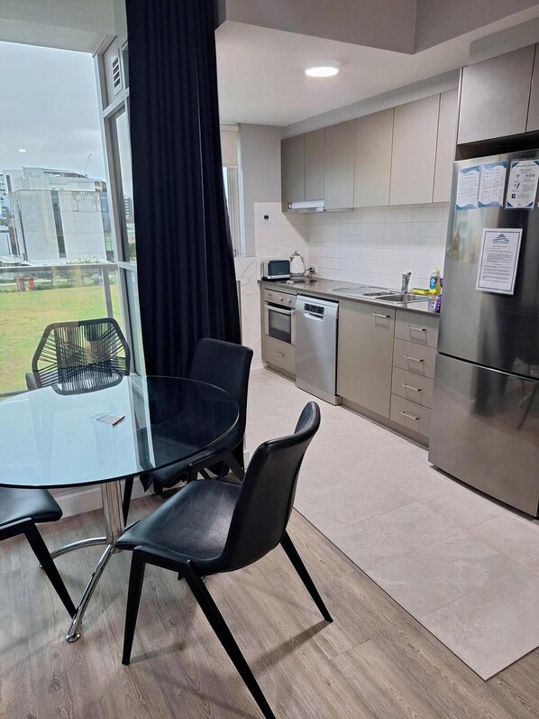 A modern kitchen with stainless steel appliances, a glass dining table, and a view of the outdoors.