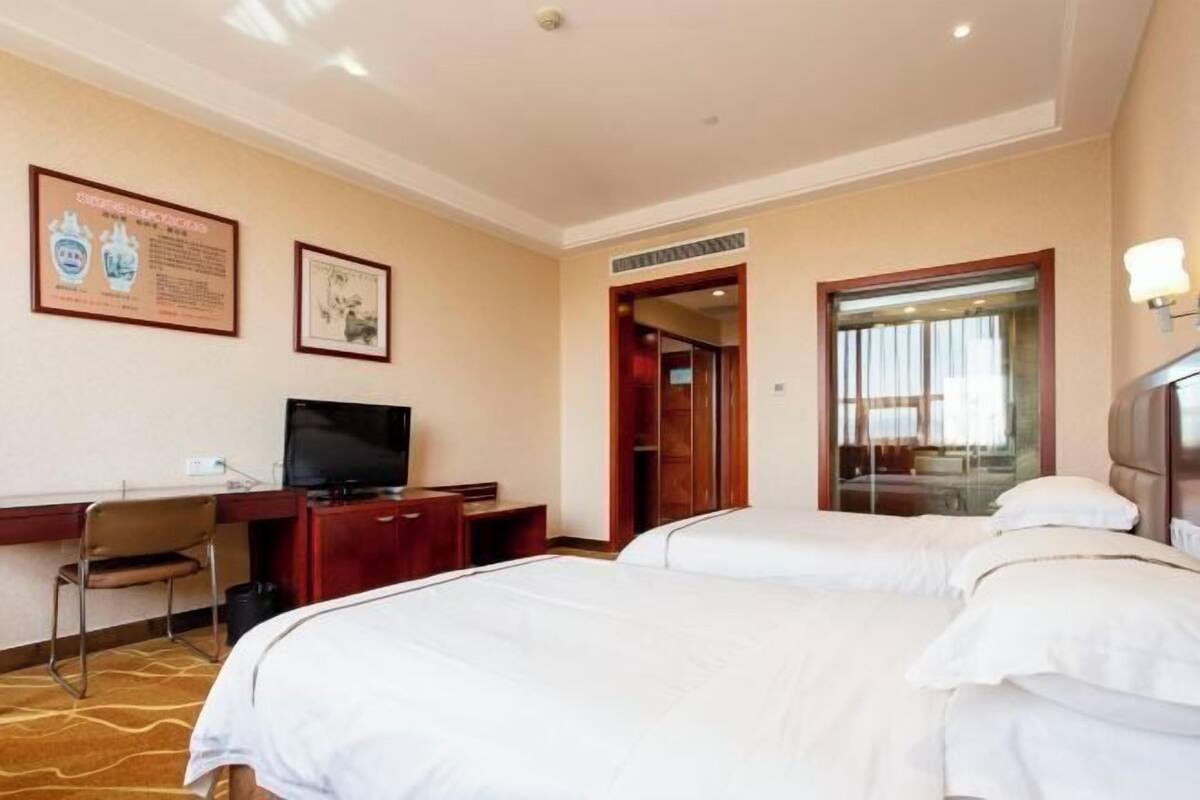A hotel room with two beds, a desk with a TV, a chair, and framed pictures on the wall.