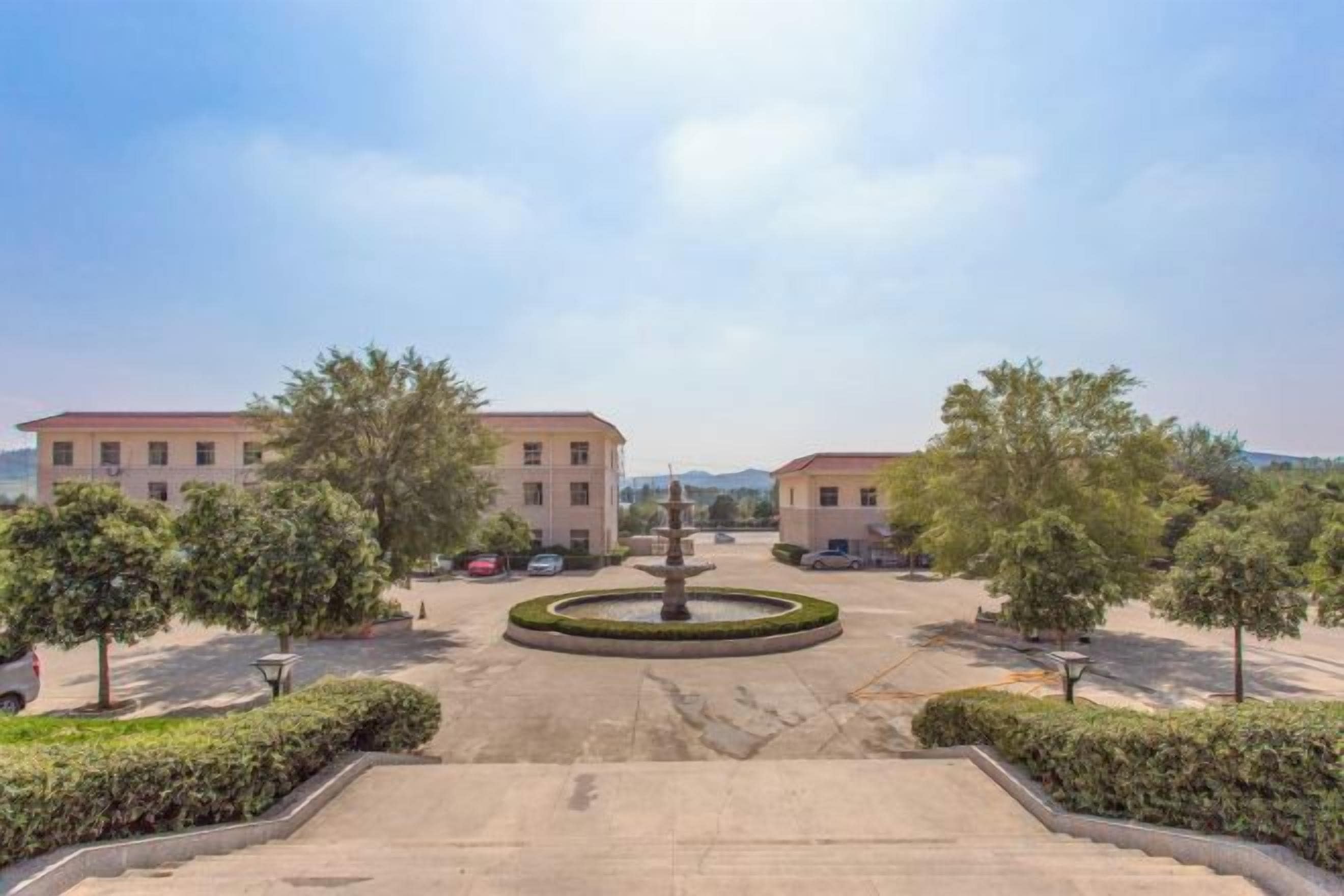 A courtyard with two buildings, a central fountain, and a clear sky.