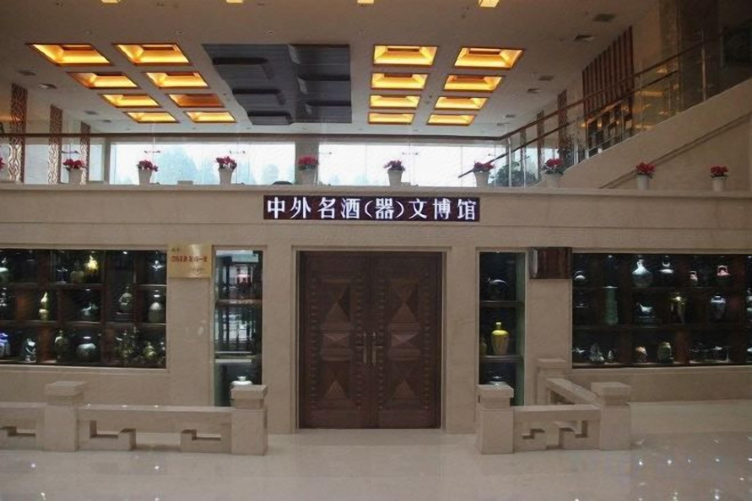 A lobby with a large wooden door, a ceiling with recessed lighting, and a balcony with potted plants.
