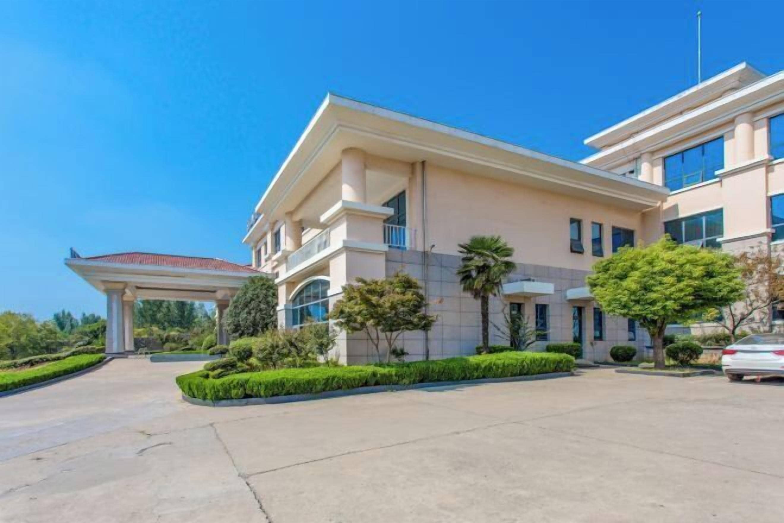 A modern hotel with a covered entrance, landscaped gardens, and a parking area.