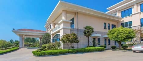A modern hotel with a covered entrance, landscaped gardens, and a parking area.
