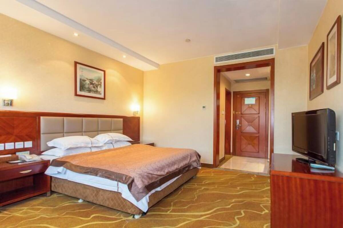 A hotel room with a bed, a television, a desk, and a door leading to another room.