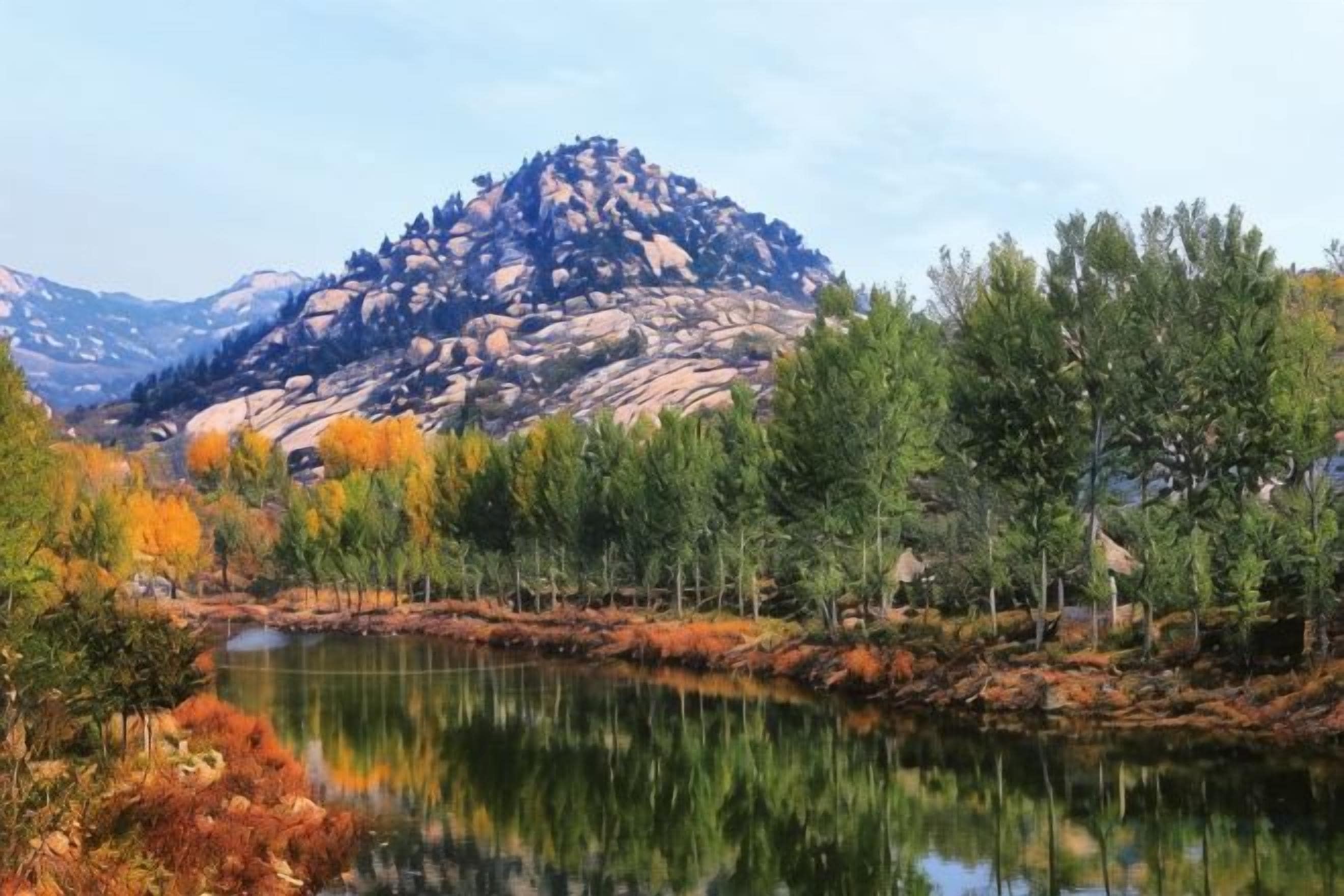 A mountainous landscape with a lake reflecting trees and a clear sky.