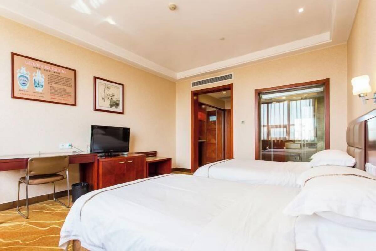 A hotel room with two beds, a desk with a television, and framed pictures on the wall.