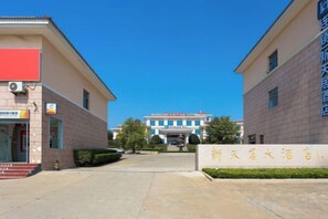 A hotel entrance with a clear sky, a signboard, and a building in the background. - Xintian Hotel (Fei County)