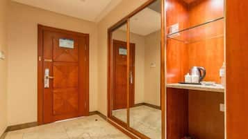 A hotel room with a wooden door, a large mirror, and a shelf with toiletries.