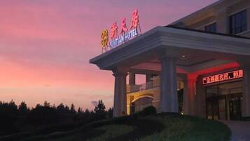 A hotel entrance with a sign indicating 'Xiantian Hotel' and a covered walkway leading to the entrance.