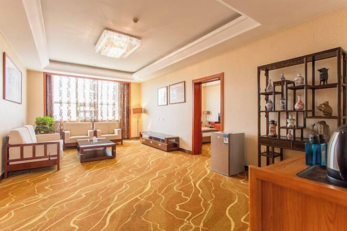 A hotel room with a sofa, coffee table, and a wooden cabinet with decorative items.