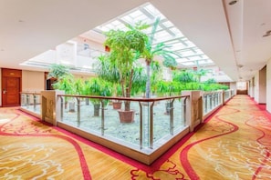 A hotel atrium with a glass floor, indoor plants, and a red carpet. - Xintian Hotel (Fei County)