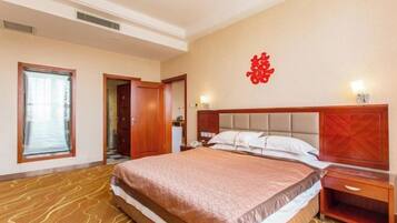 A hotel room with a large bed, a wooden headboard, a nightstand, and a wall with a red decorative element.