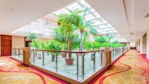 Un vestíbulo de hotel con barandilla de cristal, plantas en macetas y alfombra estampada.