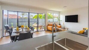 Una cocina moderna con comedor, un televisor montado en la pared y un ventanal corredero que da a un patio exterior.
