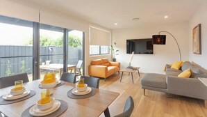 Una sala moderna con comedor, un sofá gris y un televisor montado en la pared.