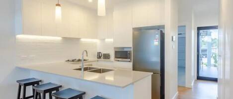 A modern kitchen with white cabinetry, a stainless steel refrigerator, a built-in microwave, and a large island with bar stools.