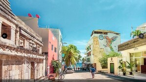 A street with buildings, including a mural, palm trees, and a clear sky. - HOSTAL DEL MAR (Playa del Carmen)