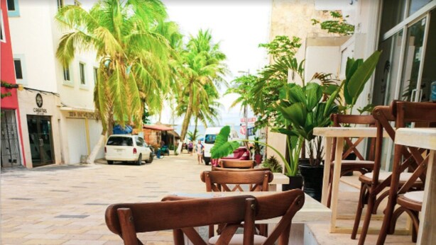 A restaurant menu with food options and prices, a white mug, and wooden chairs and tables. - HOSTAL DEL MAR (Playa del Carmen)