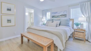 A bedroom with a bed, a bench, a ceiling fan, a window with curtains, and framed pictures on the wall. - Charming 3-bedroom house near lake in Chapin (Chapin)