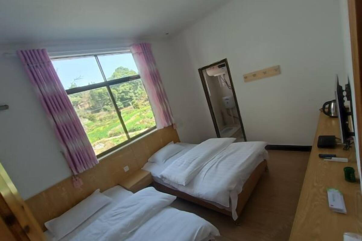 A hotel room with two beds, a wooden desk, a mirror, and a window with curtains.