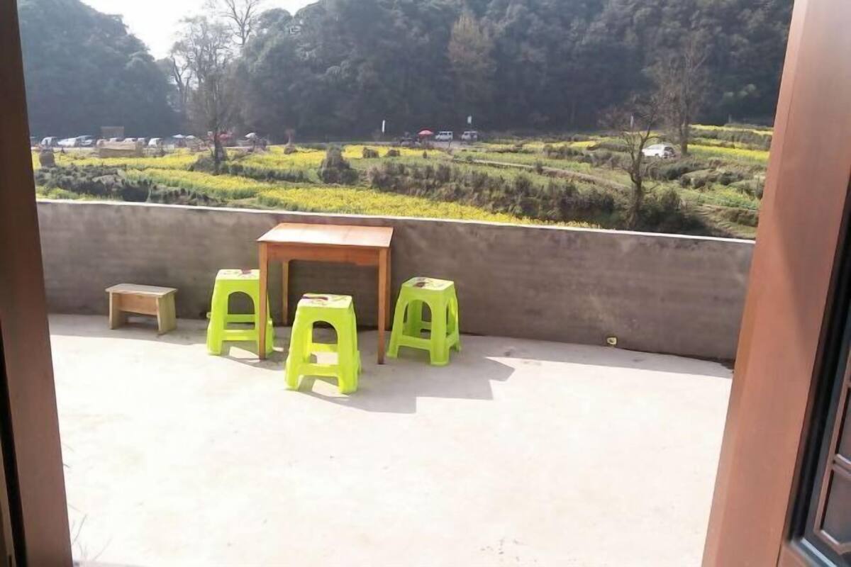 A balcony with a concrete floor, a small wooden table, and three green plastic stools.