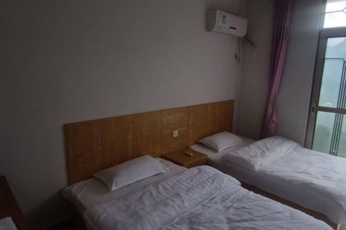 A room with two beds, a wooden headboard, a small bedside table, and a window with curtains.