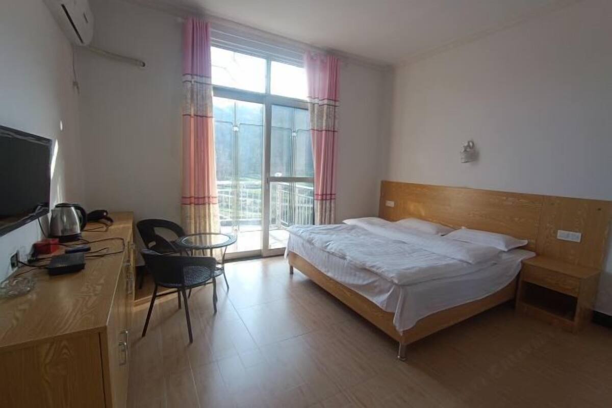 A hotel room with a bed, a desk with a chair, a TV, and a window with curtains.