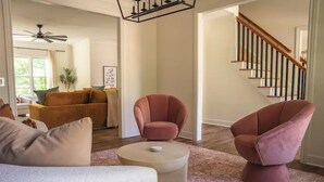 A spacious living room with a modern sofa, two armchairs, a coffee table, and a staircase with wooden railings.
